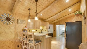 Un interior de madera con una zona de cocina que incluye armarios de madera, un taburete, un reloj y un refrigerador.