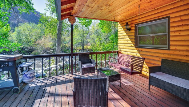 Una terraza de madera con mobiliario de mimbre, una parrilla y vistas a una montaña boscosa.