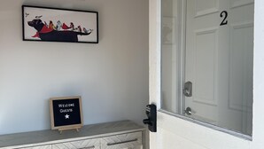 Een receptiegedeelte met een welkomstbord, een lijst, een bank en een deur met het nummer 2.