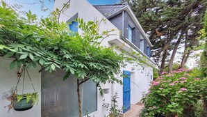 A white building with blue shutters, surrounded by greenery and a small garden with pink flowers. - 4 bedroom pet friendly home in Quiberon (Quiberon)