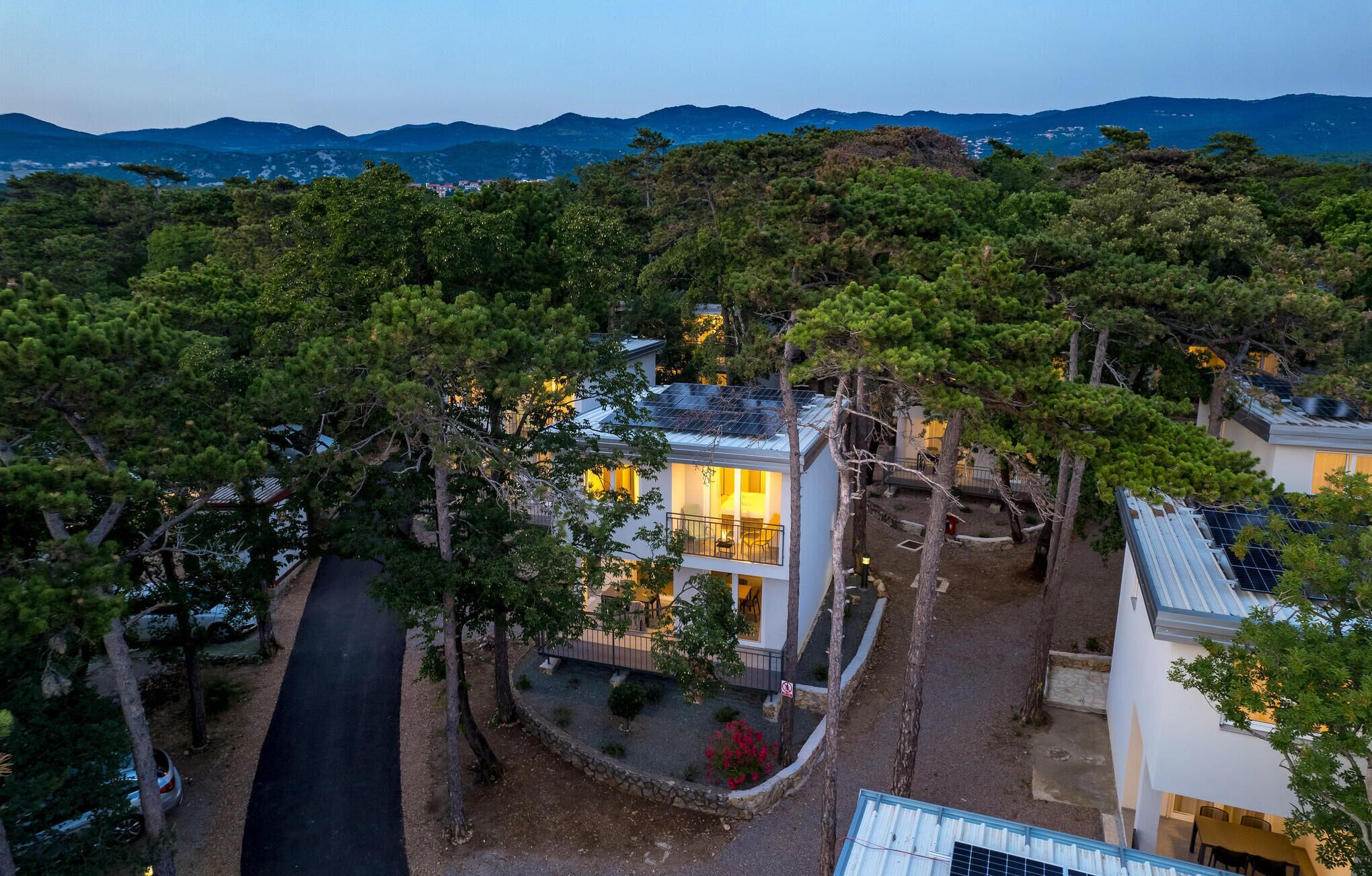 A modern house with a balcony, surrounded by trees and a mountain view.