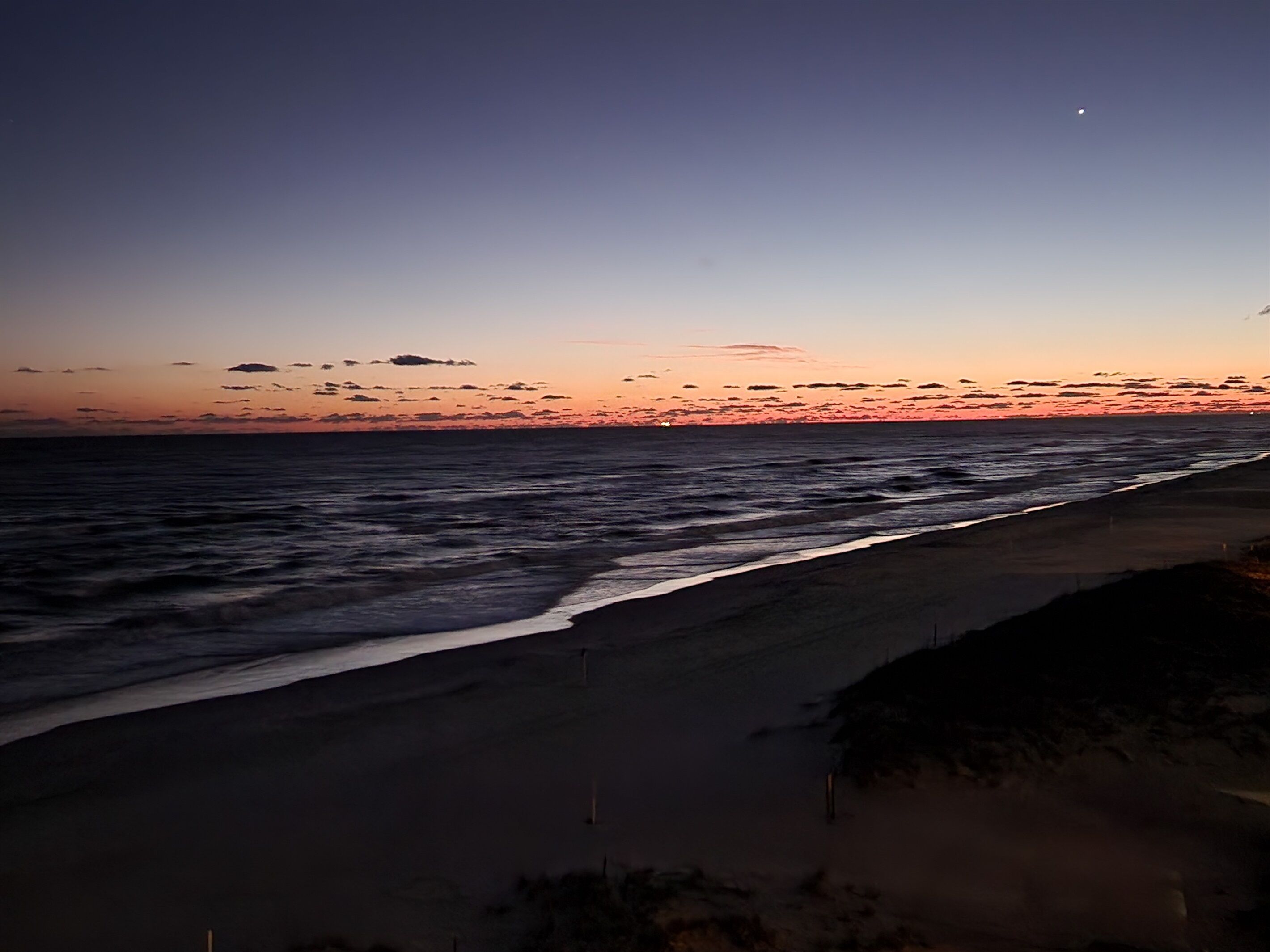 Uma praia ao pôr do sol com ondas e céu limpo.