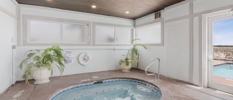 A spa area with a hot tub, potted plants, and a view of the pool outside.