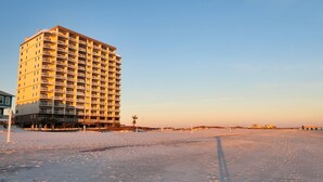 Un hotel de gran altura con varios balcones, situado cerca de una playa bajo un cielo despejado.