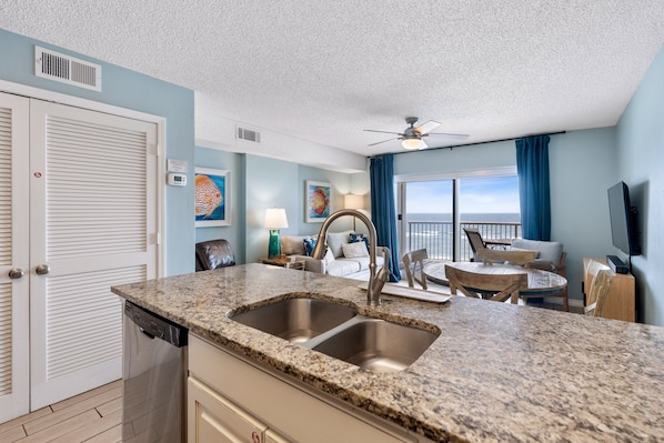 A modern kitchen with granite countertops, a double sink, and a ceiling fan. - Beachfront-Uncrowded Beach-Next to Gulf State Park-King Bed (Gulf Shores)