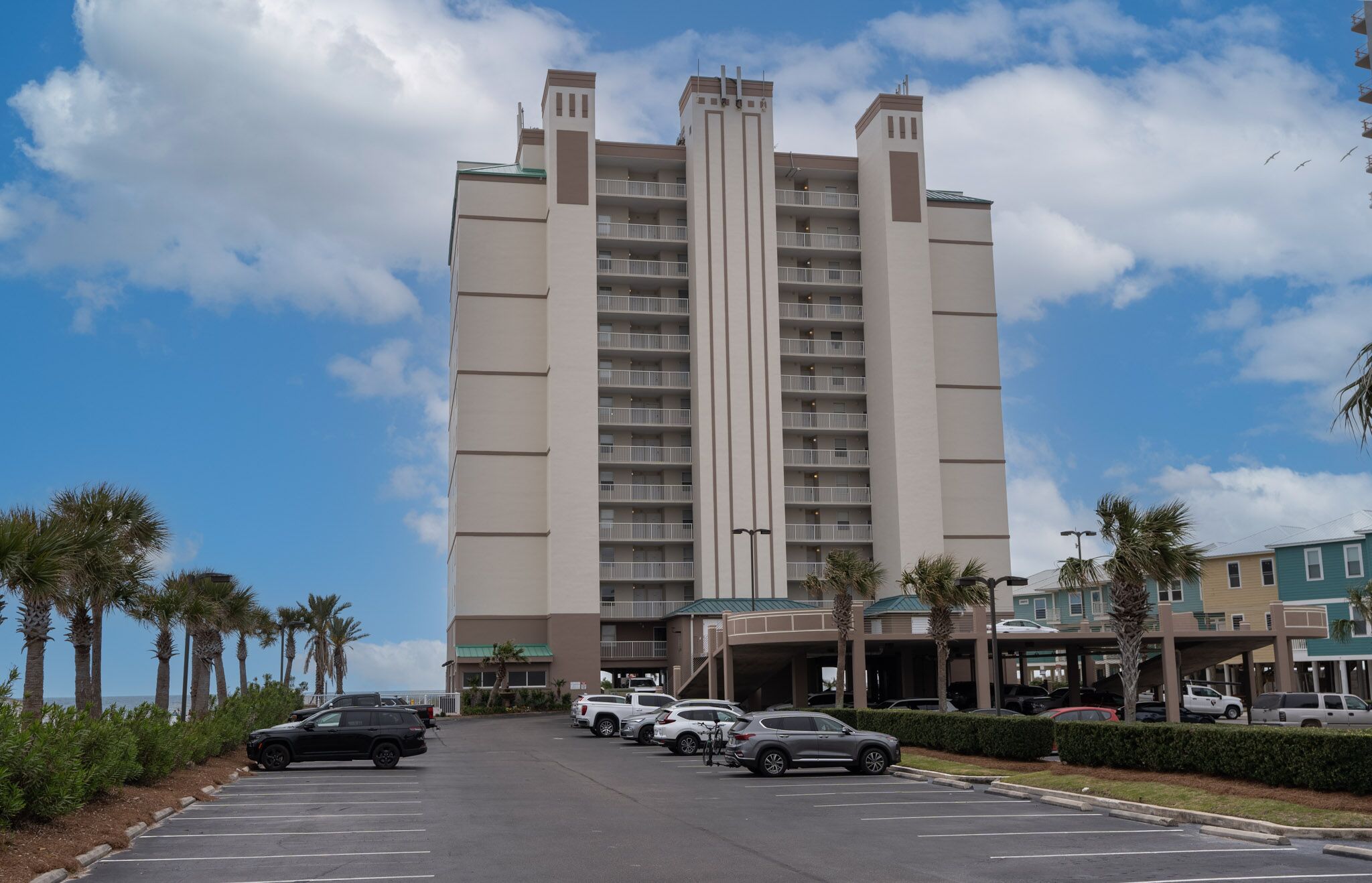A multi-story hotel with a central tower, parking lot, and surrounding palm trees.