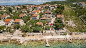 An aerial view of a coastal village with terraced houses, clear turquoise waters, and a rocky shoreline.