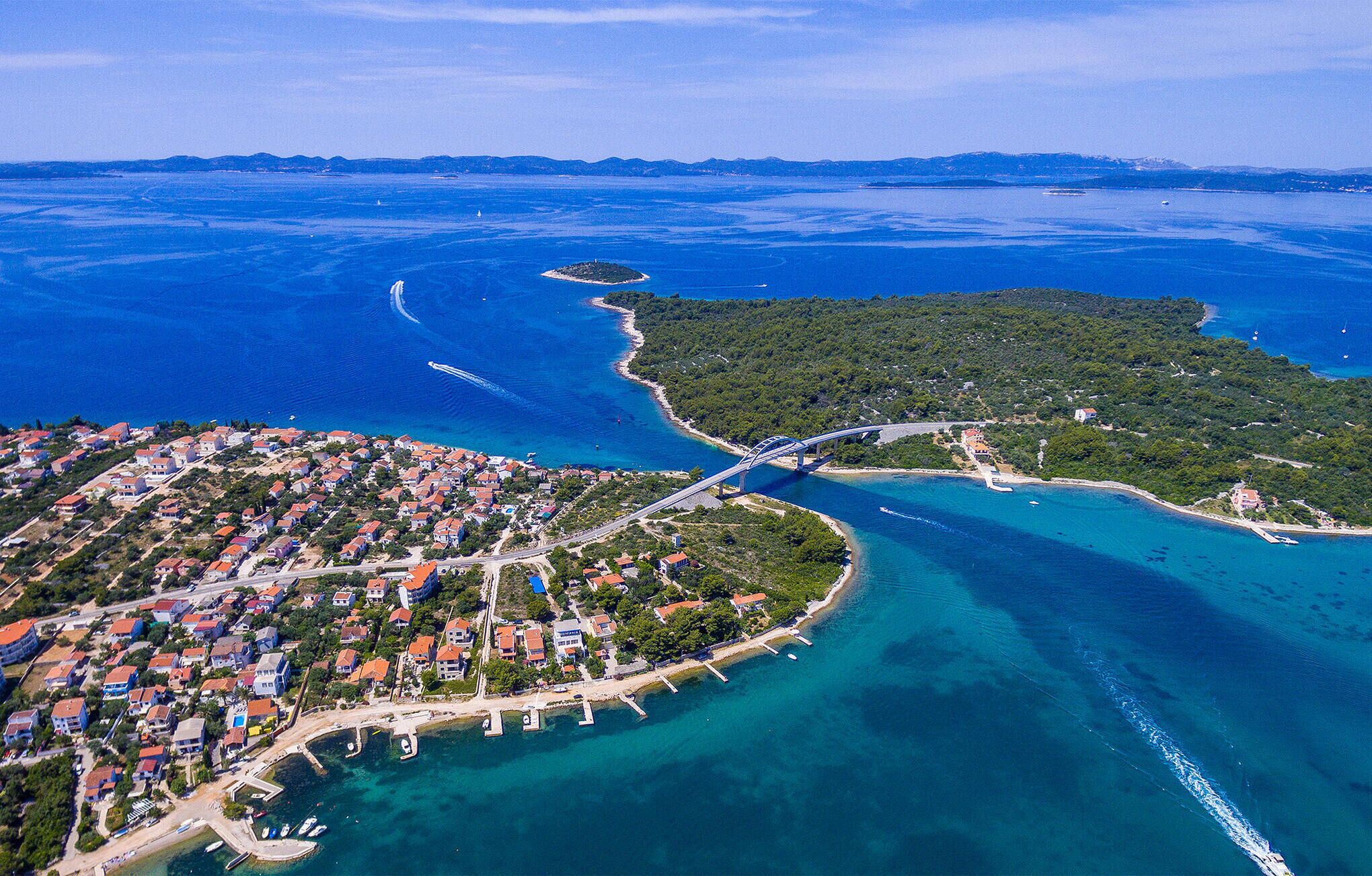 Une vue aérienne d’une ville côtière, avec un pont reliant la ville à une île, des eaux d’un bleu limpide et un mélange de bâtiments résidentiels et commerciaux.