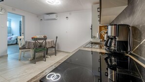 A compact kitchen with a black induction cooktop, a coffee maker, and a sink. There is a dining area with two chairs and a table, and a small kitchenette with a stove and a microwave.