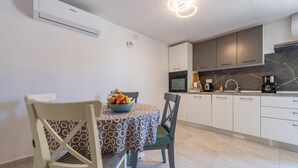 A modern kitchen with white cabinets, a marble backsplash, and a dining area with two chairs and a table.