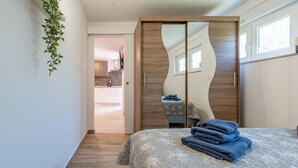 A bedroom with a bed, a mirror, and a view into the adjacent kitchen.