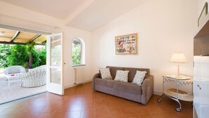 A living room with a grey sofa, a small table with a lamp, a radiator, and a window with an arched top. - 3 bedroom amazing home in Parghelia -VV- (Parghelia -VV-)