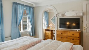 Una camera da letto con un letto, una cassettiera, una TV e una finestra con tende.