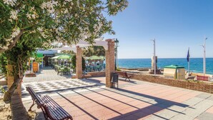 Un paseo marítimo con mesas al aire libre, un banco y vistas al mar.