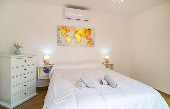 A bedroom with a bed, white dresser, two bedside lamps, an air conditioner, and a world map artwork.