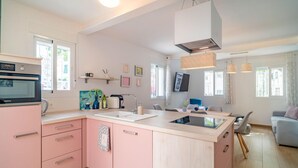 Una cocina moderna con armarios rosados, horno empotrado, un lavamanos y un comedor con mesa y sillas.
