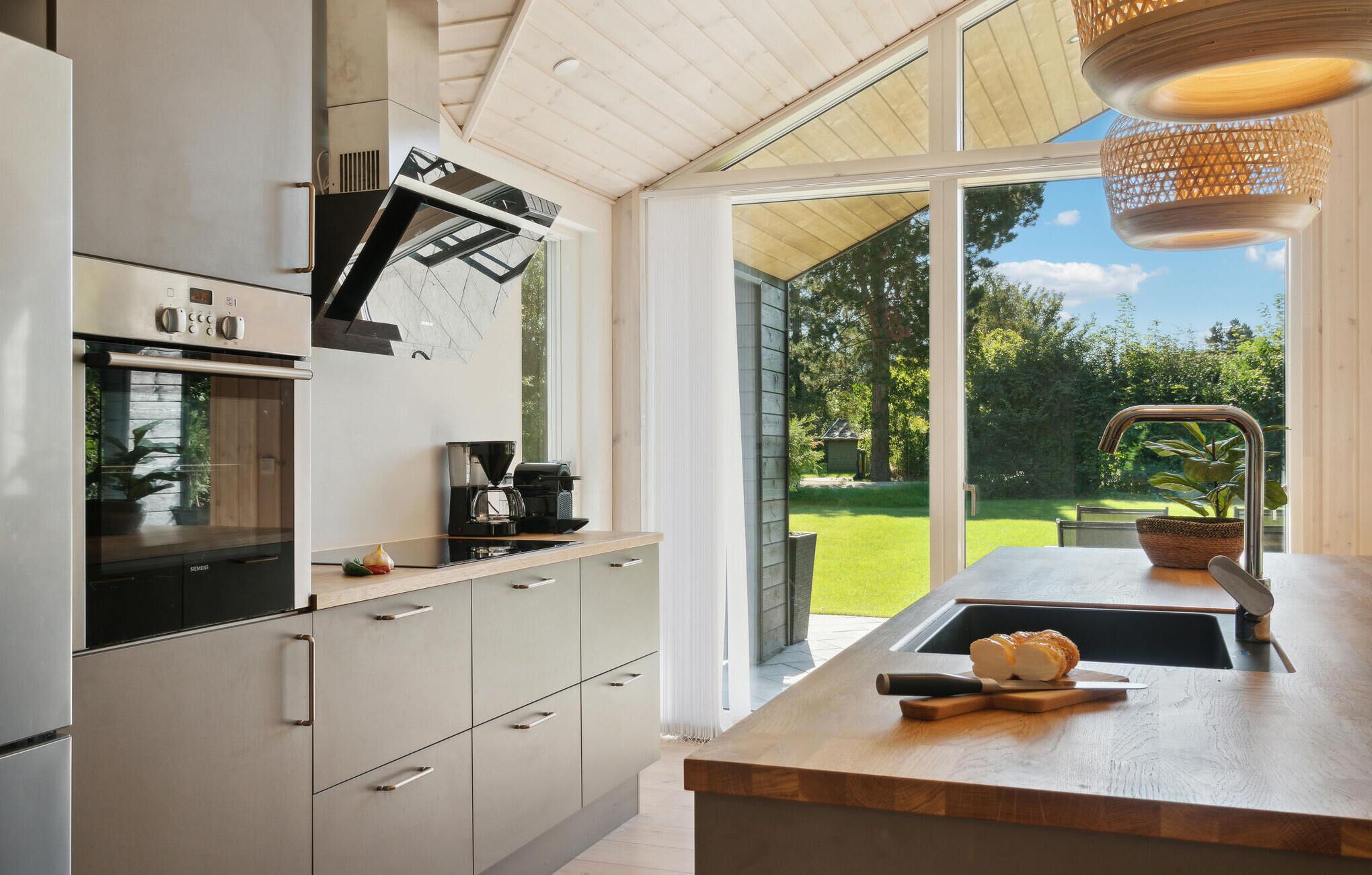 Eine moderne Küche mit Einbauofen, Kaffeemaschine und großem Fenster mit Blick ins Freie.