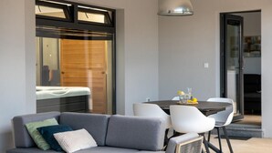 A modern living room with a grey sofa, white chairs, a round dining table, and a wooden door with a glass panel. - Awesome home in Krsan with sauna (Krsan)