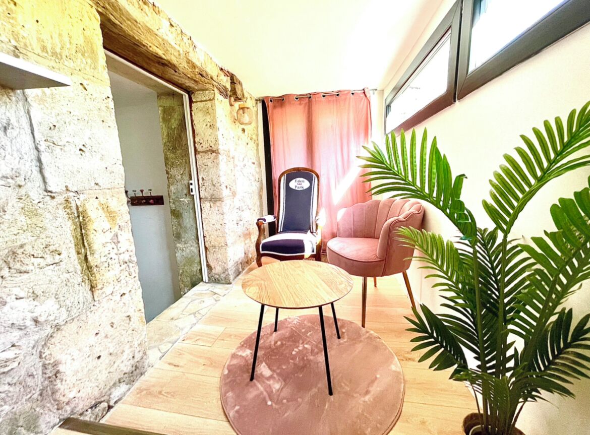A room with a stone wall, a wooden floor, a round table with a wooden top, a pink chair, and a potted plant.