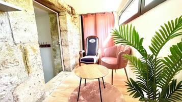 A room with a stone wall, a wooden floor, a round table with a wooden top, a pink chair, and a potted plant.