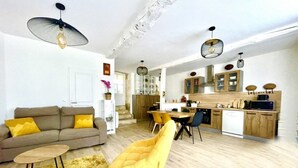 Un salon moderne avec un canapé, un fauteuil jaune et un coin repas comprenant une table et des chaises.