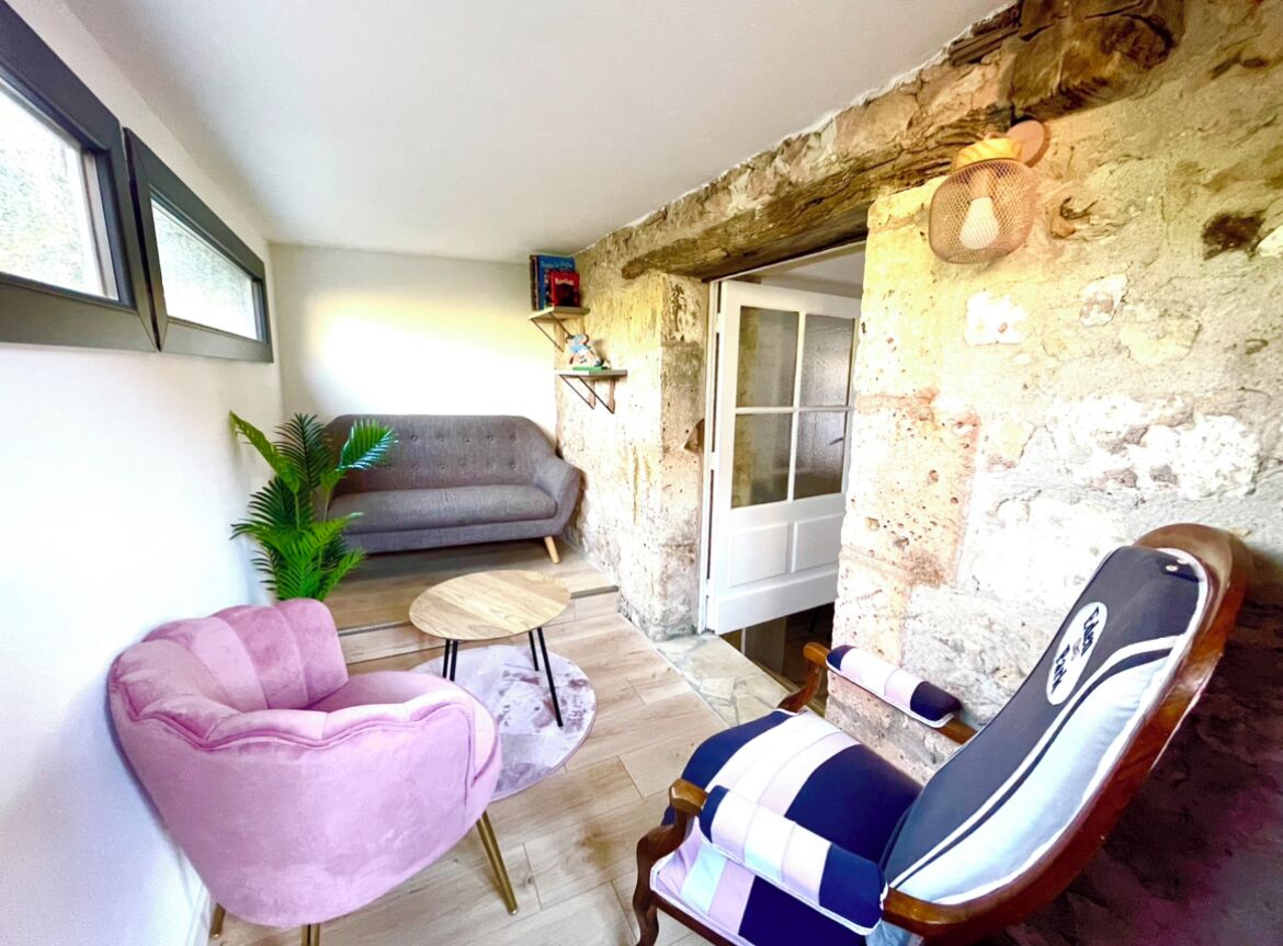 A cozy living area with a sofa, a pink armchair, a striped armchair, a small round table, and a potted plant.