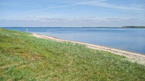 A coastal landscape with a sandy beach and grassy area leading to calm waters. - Nice home in Højslev with kitchen (Højslev)