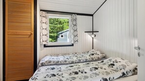 A small bedroom with two beds, a window with curtains, a wooden door, and a wall-mounted light fixture. - Nice home in Højslev with kitchen (Højslev)