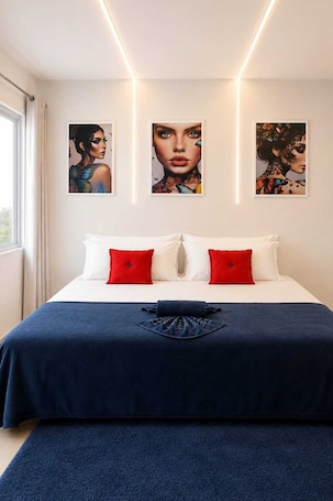 A bedroom with a bed, red and white pillows, a blue bedspread, and three framed artworks on the wall.
