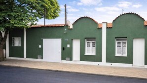 A green building with a white door, two windows with white shutters, and a tree in front. - Casa hotel Piracicaba  (Piracicaba)
