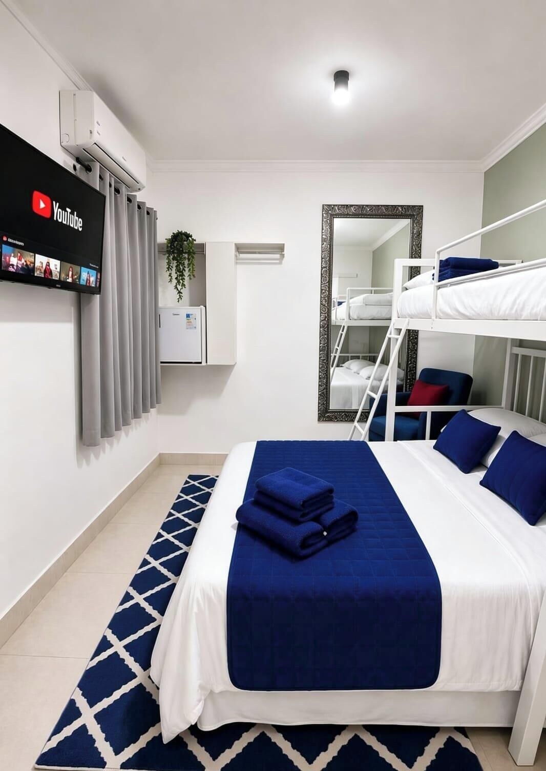 Habitación de hotel con literas, un televisor de pantalla plana montado en la pared, un espejo y una ventana con cortinas.