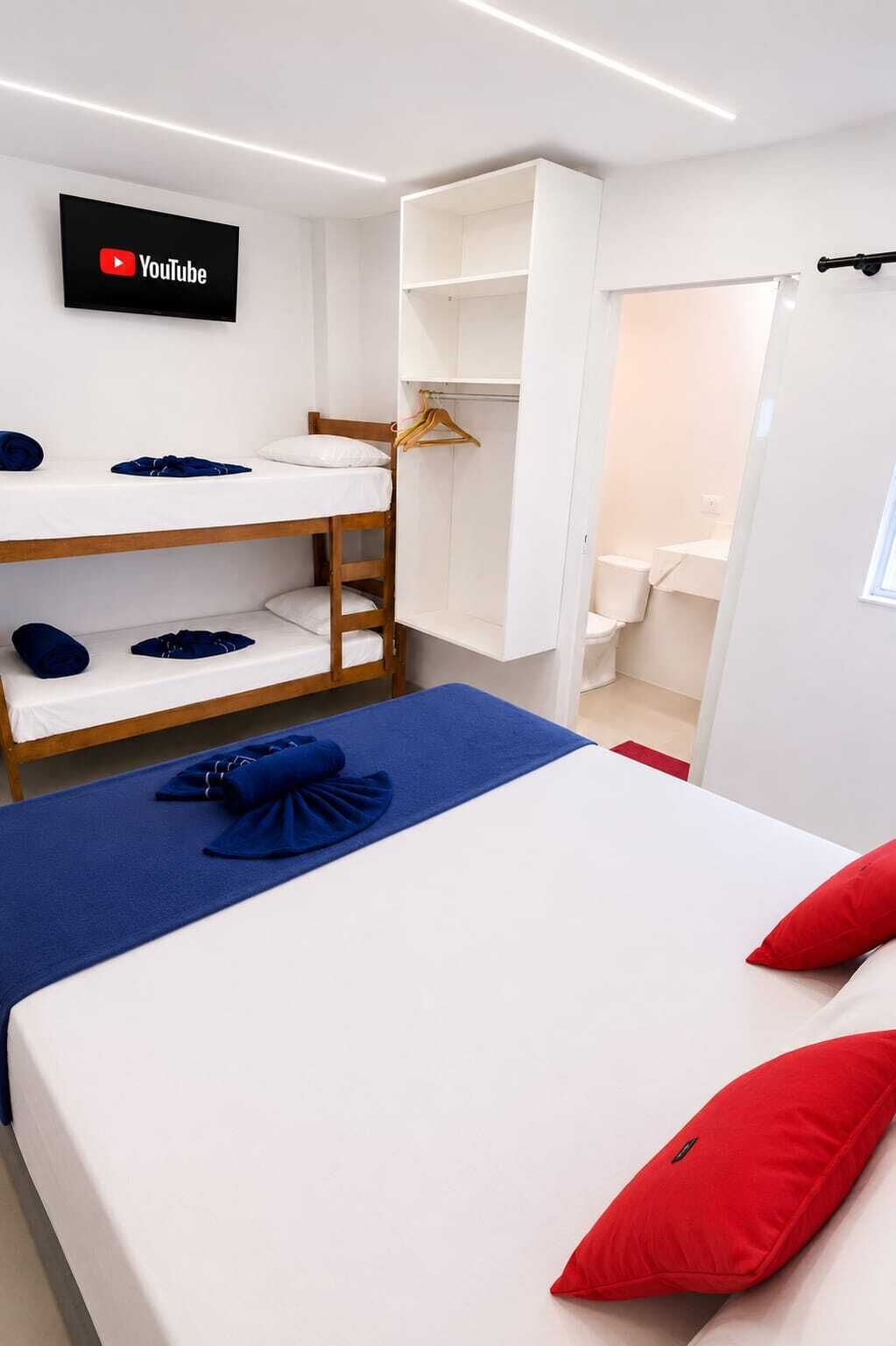 Una habitación de hotel con literas, una cama plana, un televisor montado en la pared y un armario.