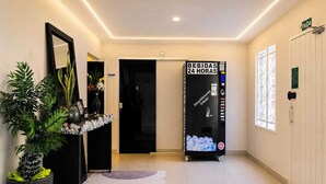 A hotel lobby with a vending machine, a reception desk, a potted plant, and a door leading to the rooms. - Casa hotel Piracicaba  (Piracicaba)