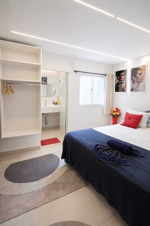 Quarto de hotel moderno com cama, closet espaçoso, banheiro e janela.