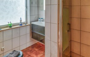 Une salle de bain avec une douche, un lavabo et une fenêtre équipée de stores.