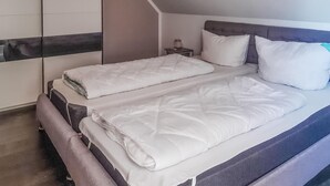 Una cama doble con ropa de cama blanca, un cabecero gris y una mesita de noche pequeña con una lámpara.