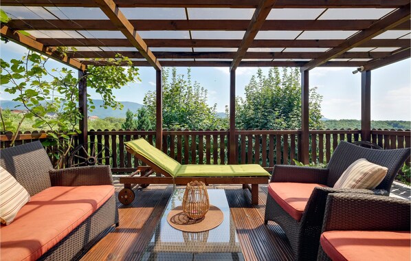 A covered outdoor seating area with wicker furniture and a glass table, overlooking a lush landscape. - Nice home in Jakovlje with sauna (Jakovlje)
