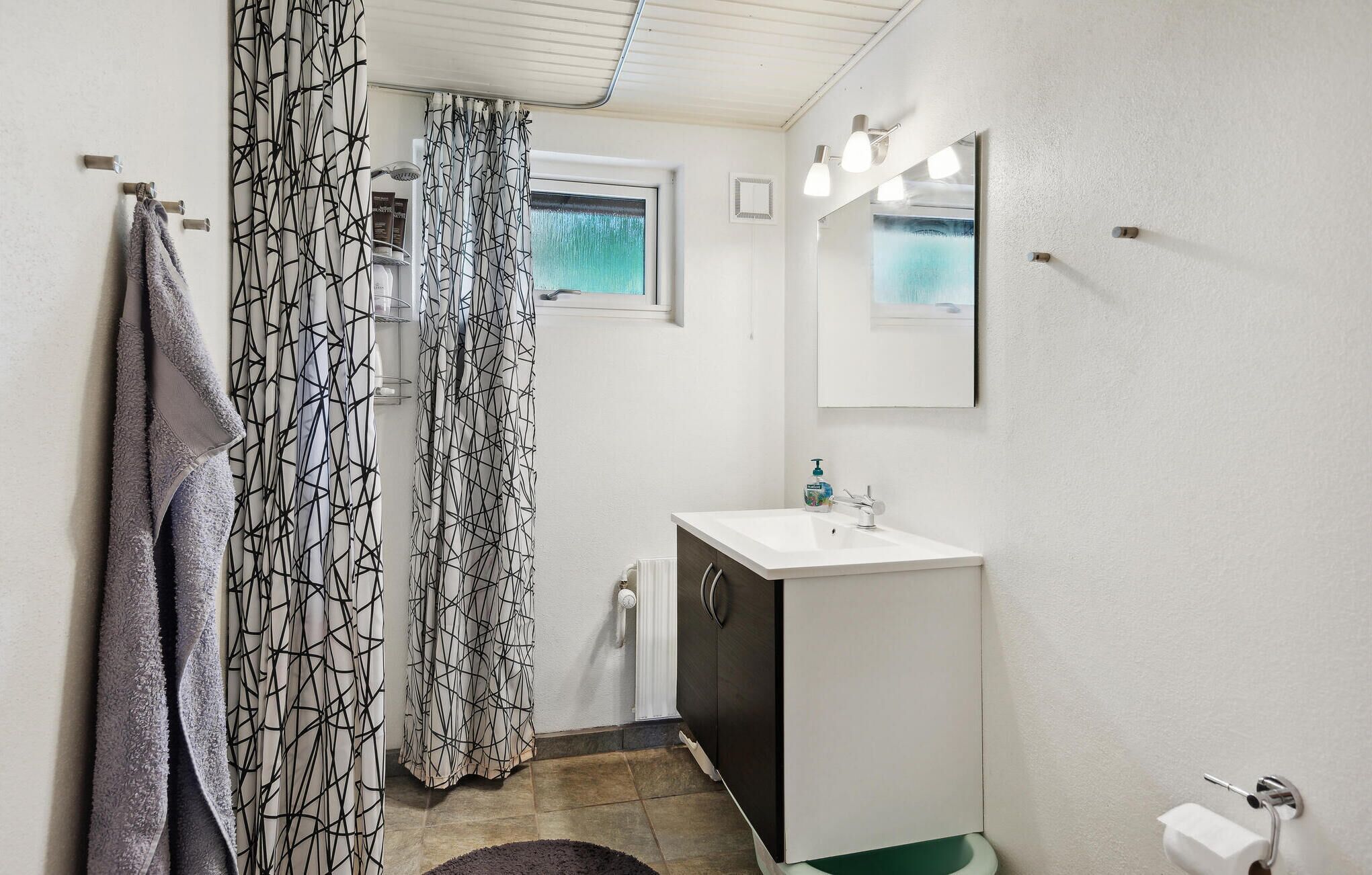 Un baño con cortina de ducha, un lavabo, un espejo y un perchero para toallas.