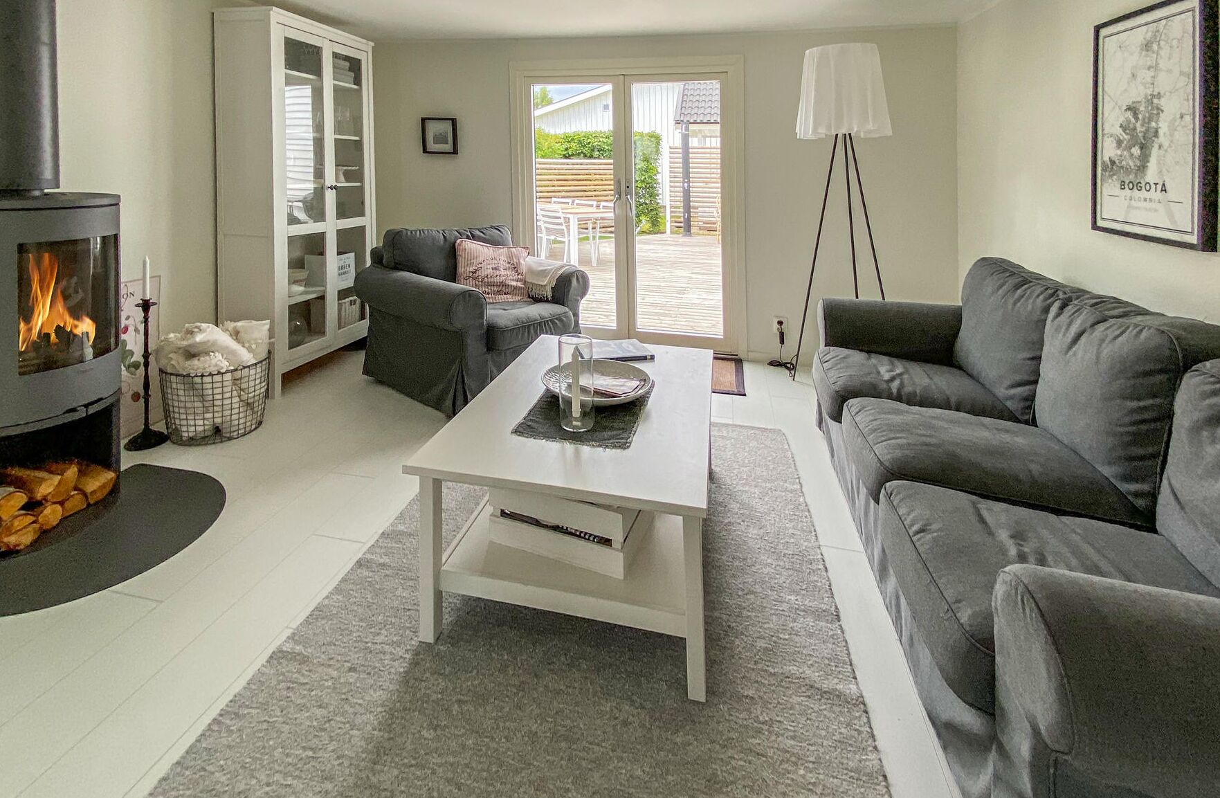 Ein modernes Wohnzimmer mit Kamin, grauen Sofas, einem weißen Couchtisch und Blick ins Freie.