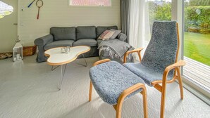 Olohuoneessa on harmaa sohva, pieni valkoinen sohvapöytä ja sininen nojatuoli. Ikkunasta avautuu näkymä vehreään maisemaan.