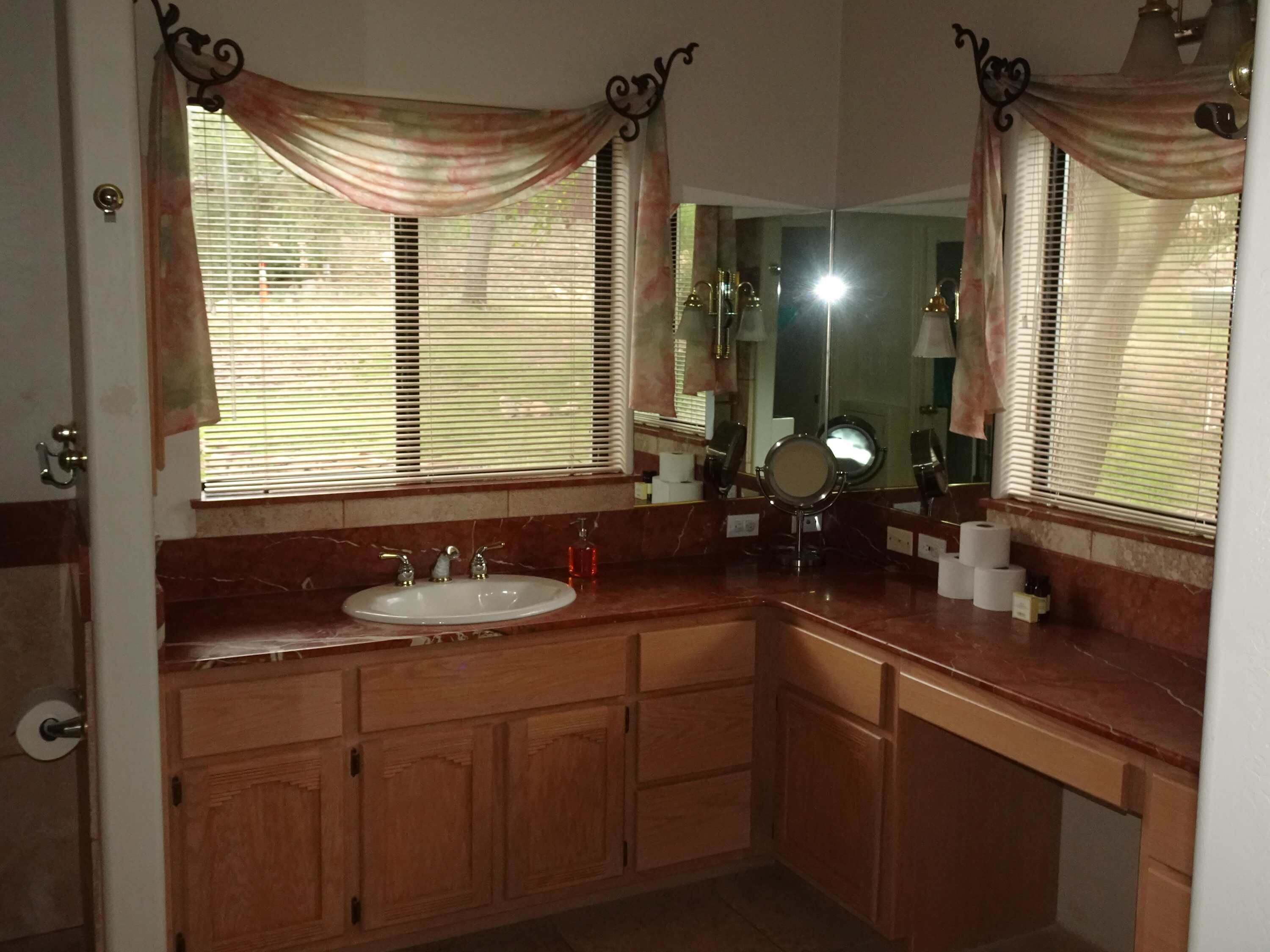 A bathroom with a sink, vanity, mirror, and window with blinds.