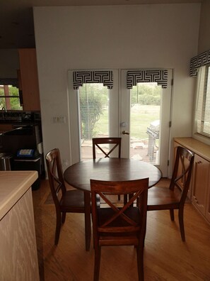 Un coin repas avec une table ronde en bois et quatre chaises, un coin cuisine avec un évier et une cuisinière, et une porte ornée de moulures d écoratives noires et blanches.