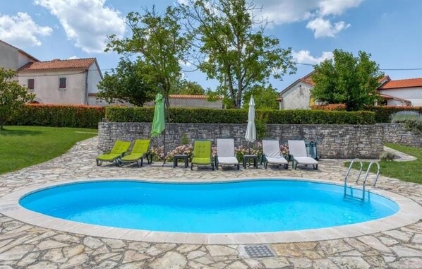 A swimming pool with lounge chairs and umbrellas, surrounded by stone walls and greenery.