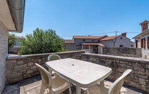 A patio with a table and chairs, stone walls, and buildings in the background.