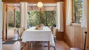 A dining area with a table set for four, surrounded by wooden walls and large windows offering a view of a forest.