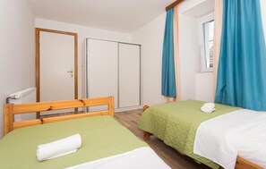A hotel room with two single beds, a wooden headboard, a radiator, and a window with curtains.