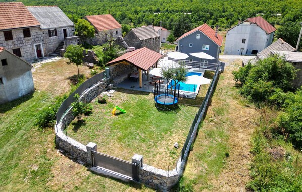 A residential area with stone houses, a swimming pool, and a trampoline.