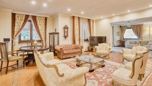 Uma sala de estar ampla com uma mesa de centro grande, poltronas elegantes e uma televisão.