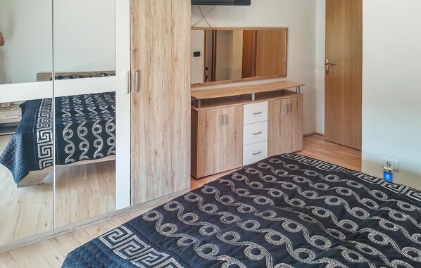 Un dormitorio con cama, armario, espejo y una mesita.