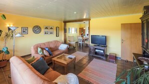 A living room with a sofa, a coffee table, a TV, and a dining area with chairs and a table.